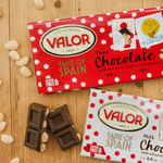 two chocolate bars on a wooded table and 2 pieces of chocolate with almonds